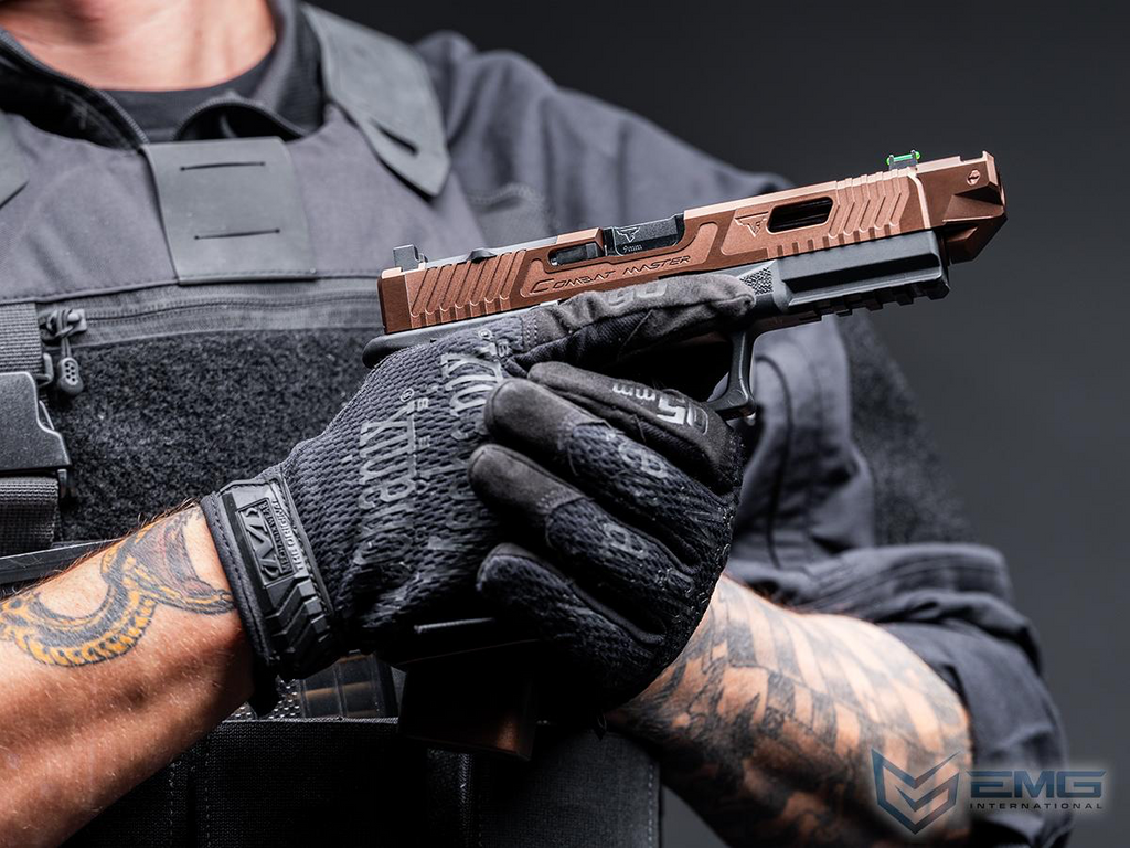 Person holding a handgun with a tactical glove, wearing a dark uniform and having tattoos on arms.