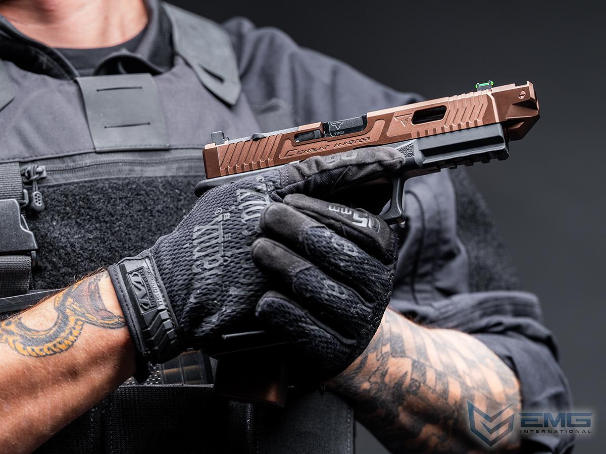 Person holding a handgun with a tactical glove, wearing a dark uniform and having tattoos on arms.