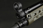 Close-up of a black tactical sight mounted on a rifle barrel, with a tan and black handguard visible against a dark background.