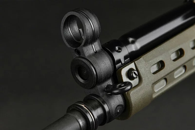 Close-up of a black tactical sight mounted on a rifle barrel, with a tan and black handguard visible against a dark background.