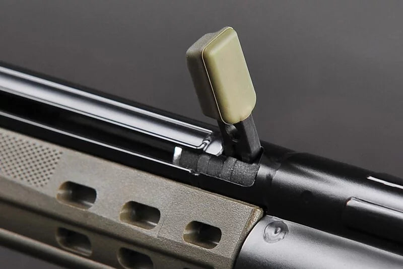 Close-up of a rifle stock and barrel area showing a tan textured foregrip and a light olive vertical sight against a dark gray background.