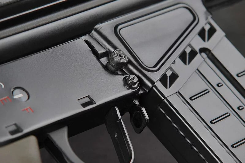 Close-up of a black tactical firearm receiver and magazine with a textured grip and small red markings.