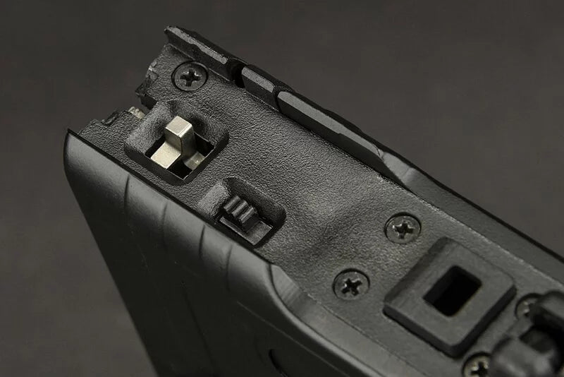 Close-up detail of a black textured plastic component with screws, a small metal switch, and a rectangular slot, shown against a dark gray background.