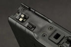 Close-up detail of a black textured plastic component with screws, a small metal switch, and a rectangular slot, shown against a dark gray background.