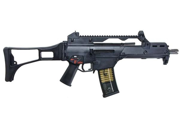 A black VFC G36c with a collapsible stock, vertical foregrip, and a gold-colored magazine, shown against a plain white background.