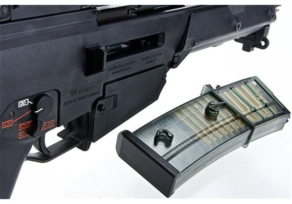 A close-up of a black firearm receiver and magazine assembly on a white background, with a translucent magazine containing green-tinted cartridges shown in front.