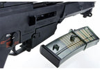 A close-up of a black firearm receiver and magazine assembly on a white background, with a translucent magazine containing green-tinted cartridges shown in front.