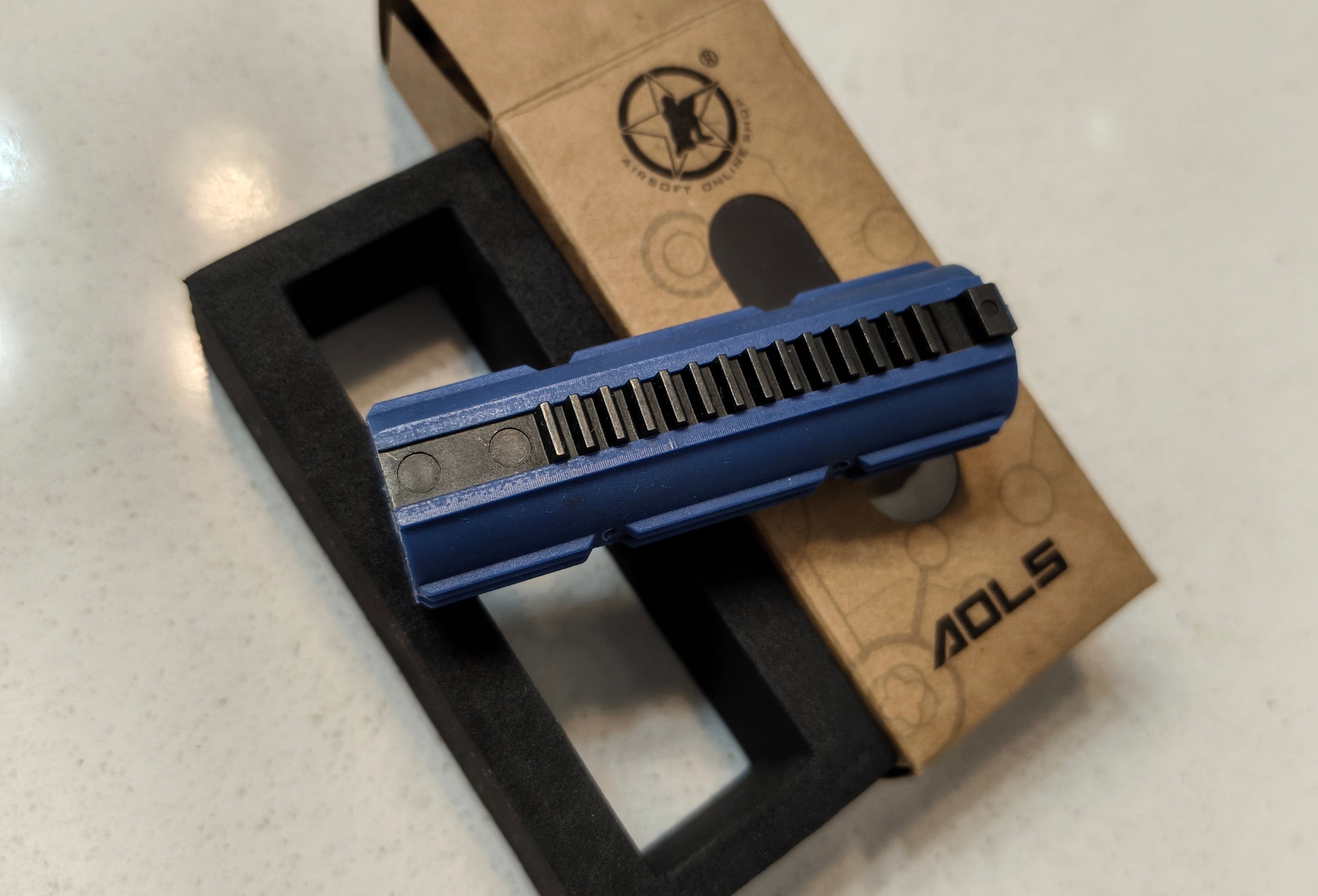 Blue metal component on a black stand with a cardboard box in the background